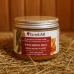 Pirts medus “Mežs” no farmLAB plastmasas traukā ar baltu vāku, novietots uz salmiem pirts interjerā