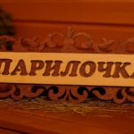 Koka dekoratīva pirts izkārtne ar uzrakstu “Парилочка”, novietota uz lāvas