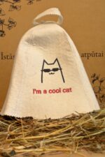 Balta filca pirts cepure ar uzrakstu “I’m a cool cat”, skats no sāniem, novietota uz salmiem uz kartona pamatnes