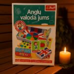 Galda spēles kaste “Angļu valoda jums” novietota uz koka lāvas pirts telpā, blakus degoša svece