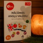 Galda spēles kaste “Mācāmies angļu valodu” uz koka virsmas pirts telpā, fonā redzama sāls lampa