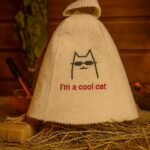 Balta filca pirts cepure ar uzrakstu “I’m a cool cat”, skats no priekšpuses, novietota uz salmiem uz kartona pamatnes