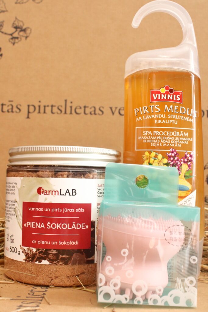 Pirts dāvanu komplekts ar pirts medu, vannas sāli un kosmētikas līdzekli, novietots uz salmiem