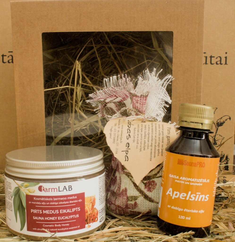 Dāvanu komplekts pirtij ar pirts medu eikalipta svaigumam, apelsīna gaisa aromatizētāju un tekstila maisiņu, novietots uz salmiem