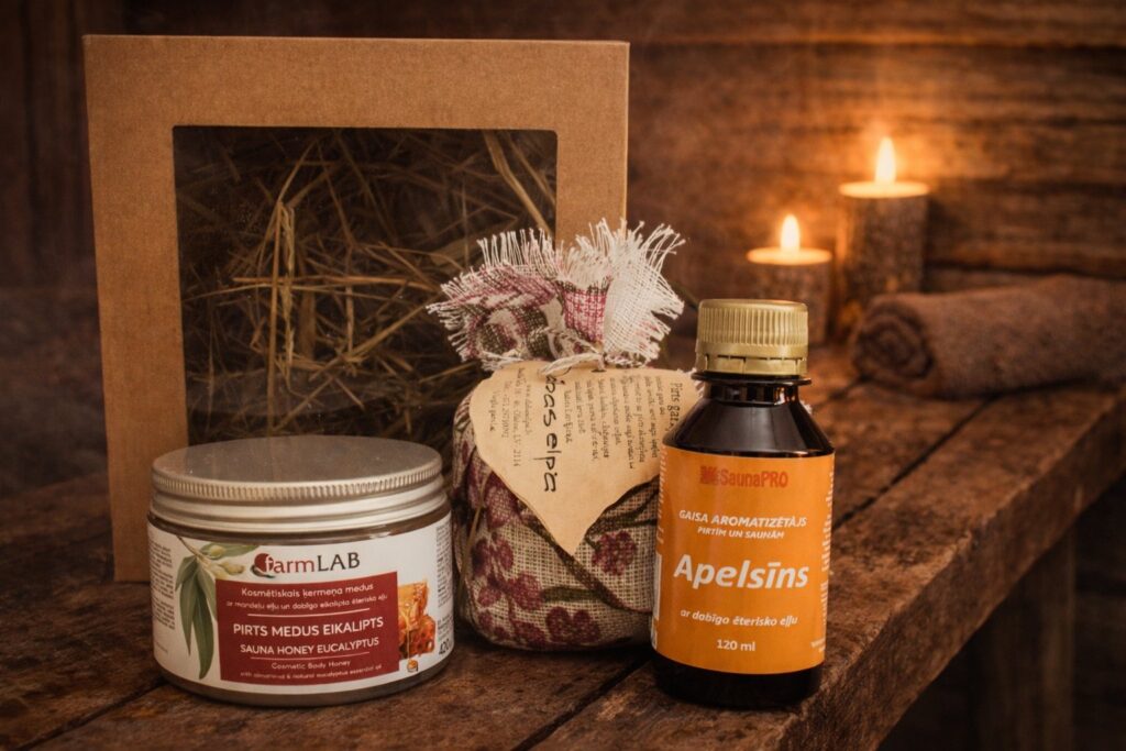 Iepakots dāvanu komplekts pirtij ar pirts medu eikalipts, apelsīna gaisa aromatizētāju un tekstila pirts gariņu, novietots uz koka lāvas pirts interjerā
