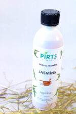 Pirts aromāts “Jasmīns” baltā pudelē ar melnu vāciņu, novietots uz salmu klājuma gaišā fonā