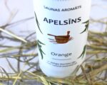 Saunas aromāts “Apelsīns” baltā pudelē tuvplānā uz gaiša salmu klājuma