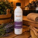 Pirts lāvu mazgāšanas līdzeklis ar lavandas aromātu 500 ml baltā pudelē novietots uz koka lāvas pirts interjerā. Blakus redzami lavandas ziedi, koka pirts spainis, pirts krāsns akmeņi un pirts birste.