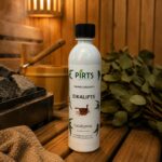 Pirts aromatizators ar eikalipta aromātu 500 ml baltā pudelē novietots uz koka lāvas pirts interjerā. Fonā redzama pirts krāsns ar akmeņiem, koka spainis un eikalipta zari.