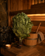 Ievas pirts slota novietota uz koka lāvas tradicionālā pirts interjerā. Blakus redzams koka ķipis, pirts akmeņi, degoša svece un trauks ar kaltētām Ievas lapām.
