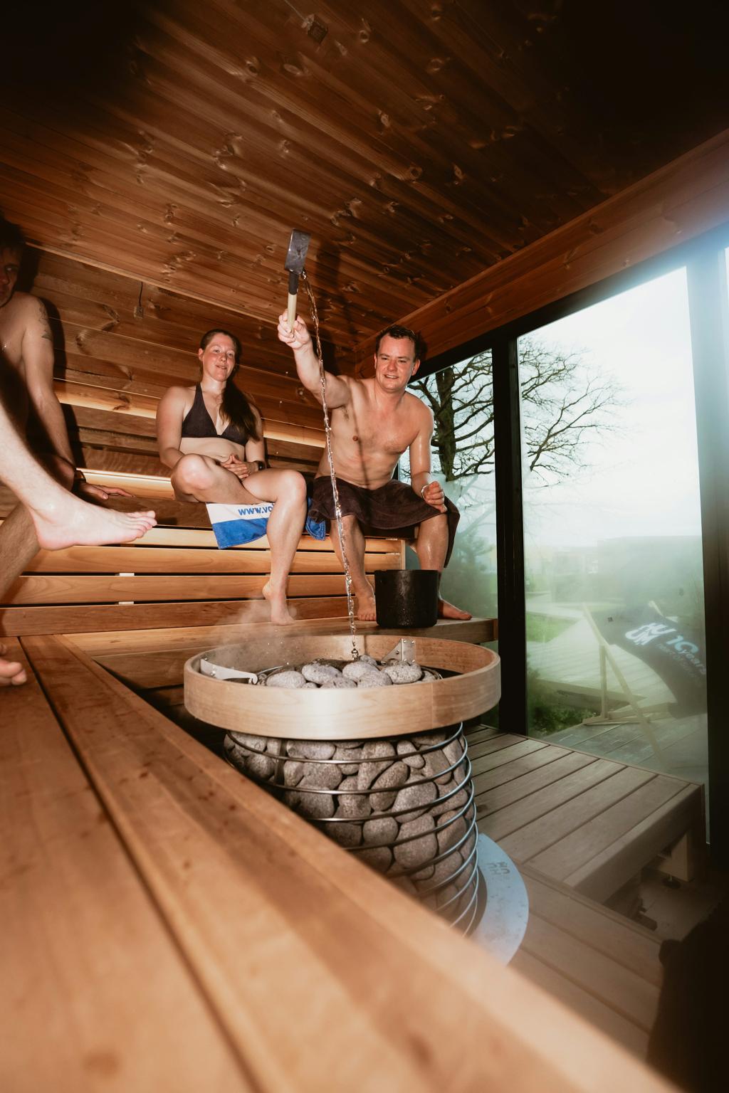 Cilvēki koka saunā pie akmeņu krāsns Sauna Theatre Edinburgh pasākuma laikā.